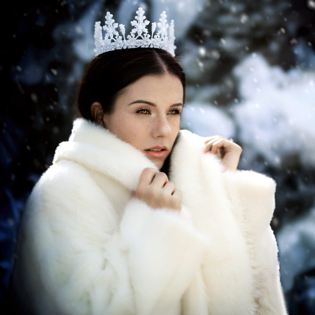 A person wearing a white fur coat and a decorative crown stands in a snowy environment, captured beautifully by Pixelhaus Photography.